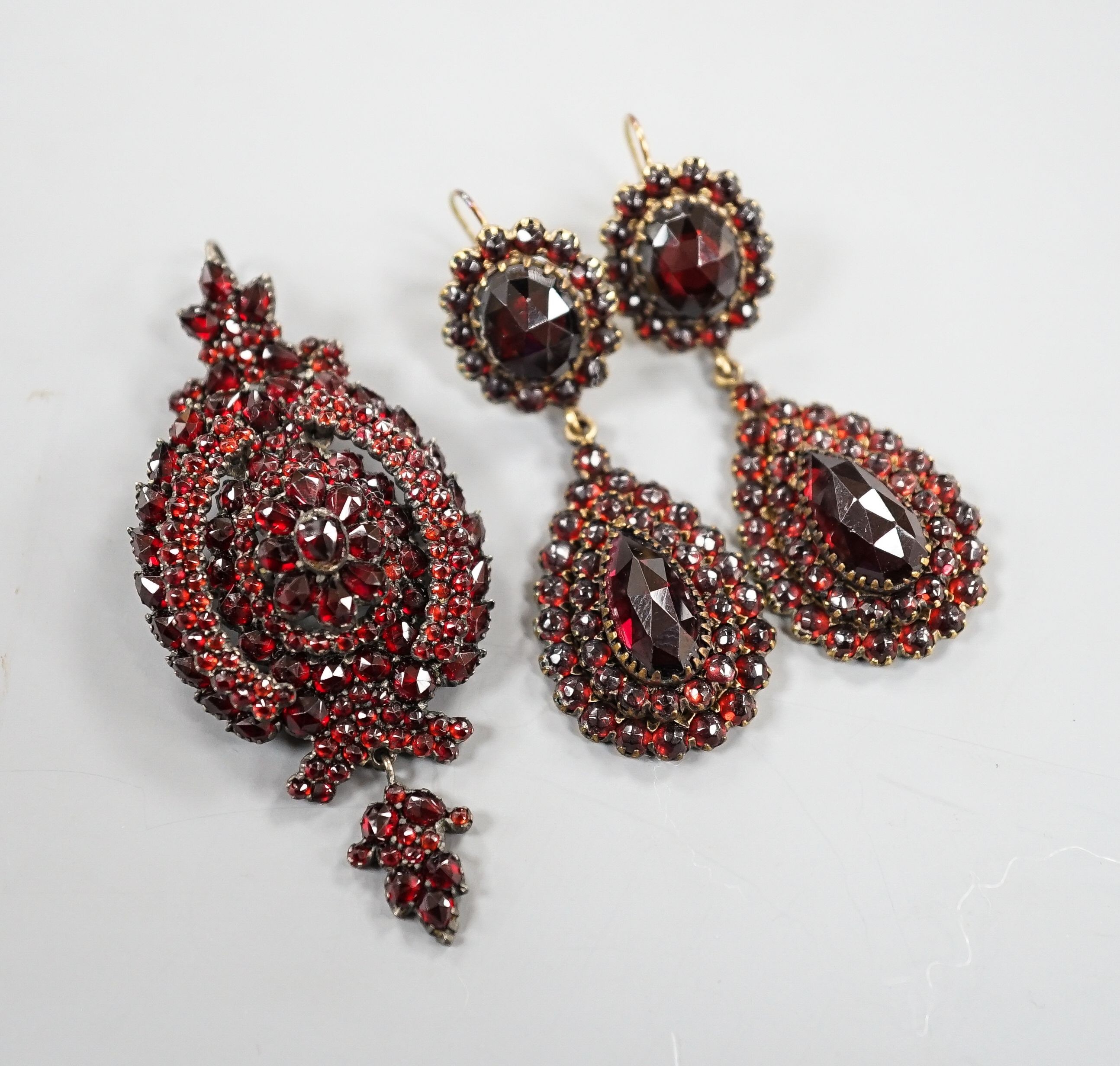 A pair of Victorian gilt metal and facet cut garnet set drop earrings, 51mm and a similar white metal and garnet set pendant brooch.
